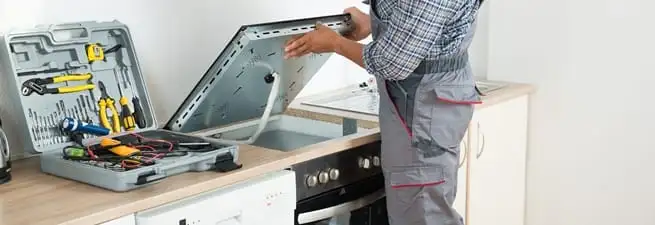 Cooktop repair technician lifting a built-in stovetop for service in Boise, ID