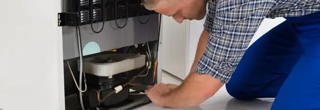 Refrigerator repair technician servicing the compressor and condenser area in Boise, ID