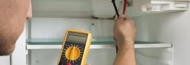 Refrigerator repair technician testing electrical components with a multimeter in Boise, ID